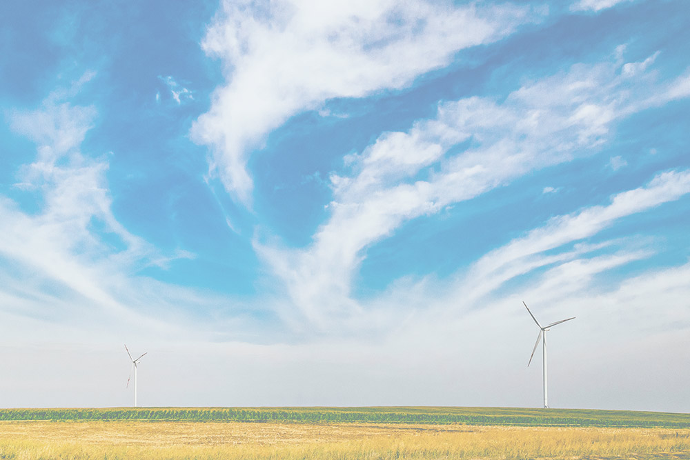 Image of windmils in a field on a clear blue day with some clouds in the sky.